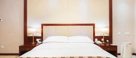 Quarto de hotel com uma cama grande, duas mesas de cabeceira, um criado-mudo, uma lâmpada, um telefone e um aquecedor.