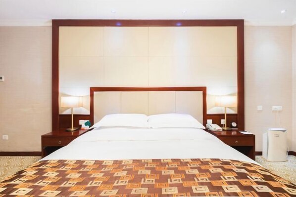 Quarto de hotel com uma cama grande, duas mesas de cabeceira, um criado-mudo, uma lâmpada, um telefone e um aquecedor.