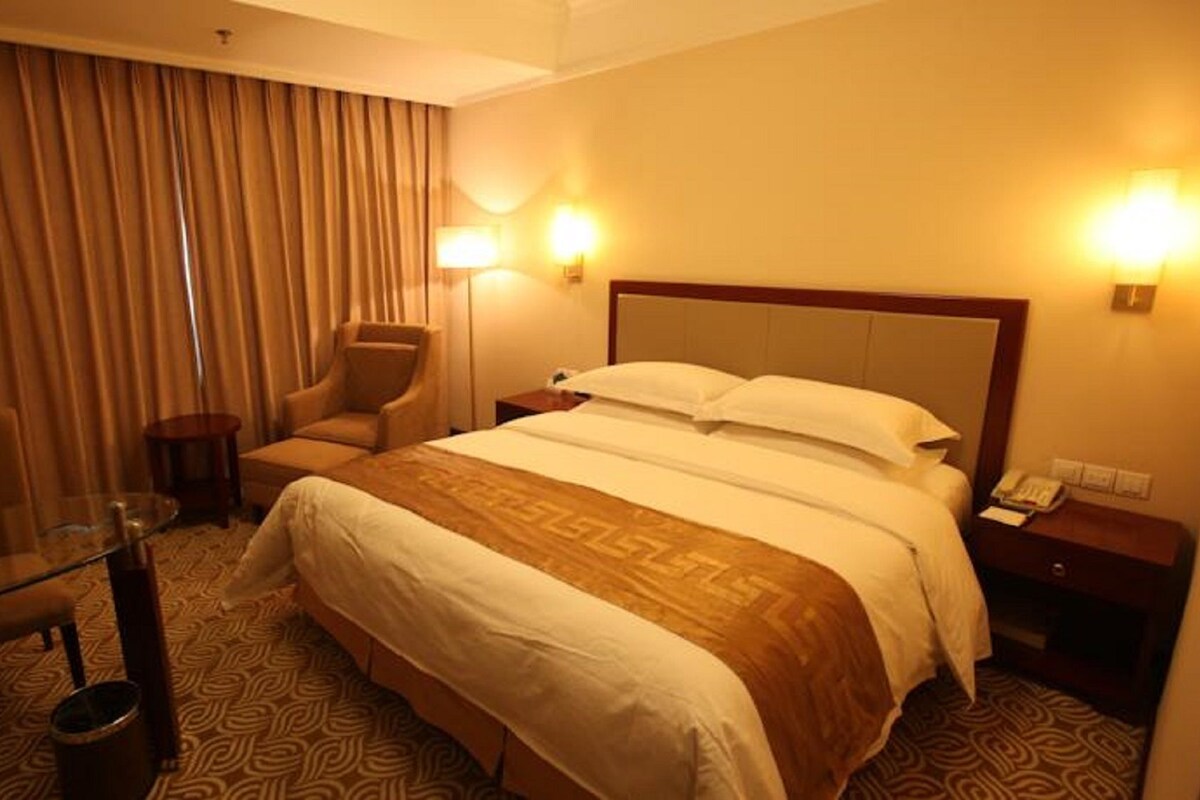 A hotel room with a bed, a chair, a small table, and a lamp.