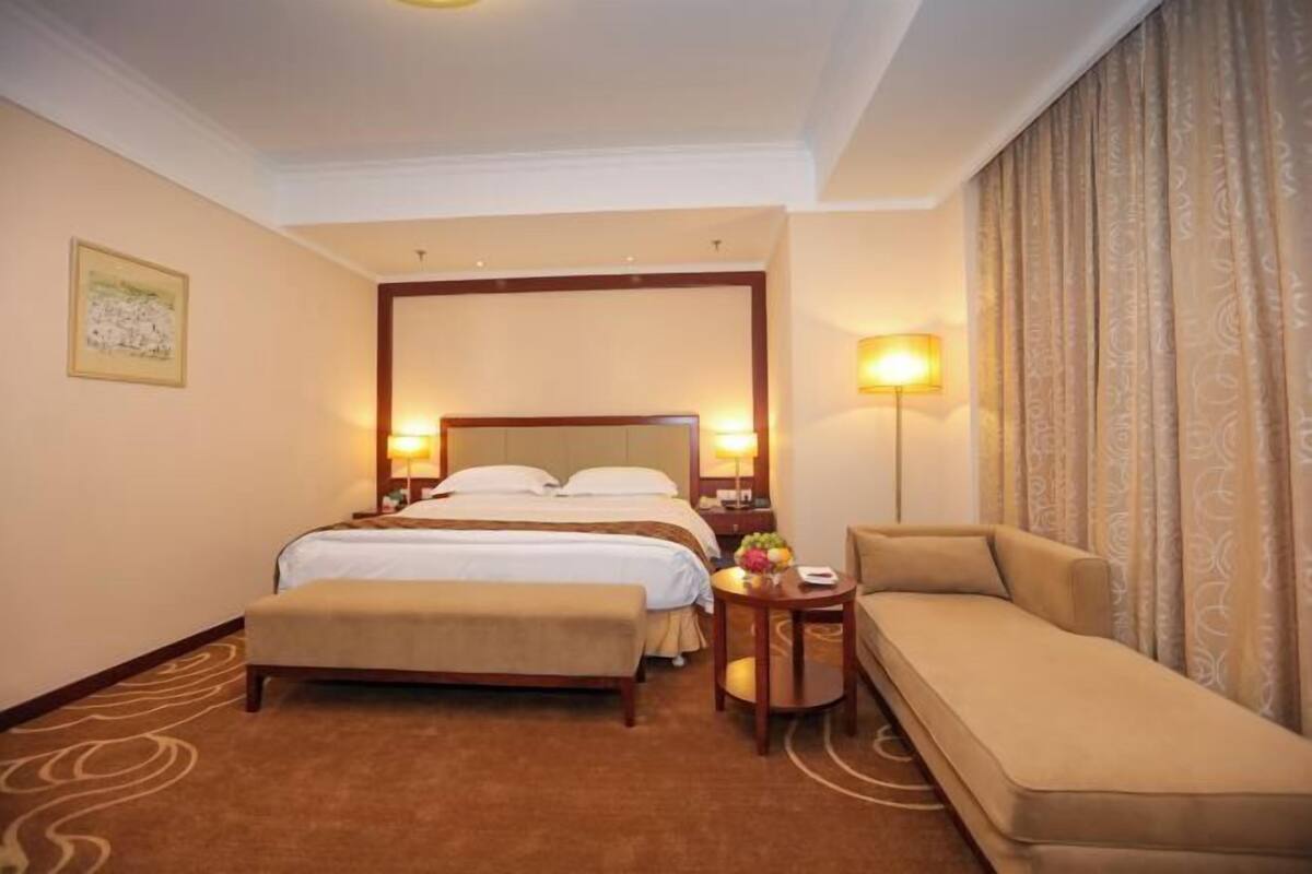 Une chambre d’hôtel avec un lit double, une table de chevet avec une lampe, un canapé et une petite table avec des fruits.