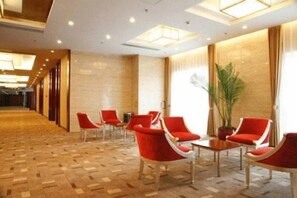 A hotel lobby with a wooden parquet floor, red chairs, a potted plant, and a large window with curtains.