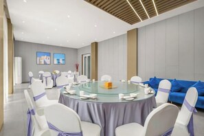Une salle de conférence avec une table ronde, des chaises blanches ornées de rubans violets et un canapé bleu.