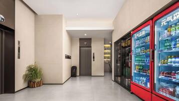 A hallway with vending machines, a potted plant, and a door leading to another room.