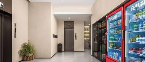 A hallway with vending machines, a potted plant, and a door leading to another room.