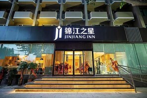 Entrada d'hotel amb un rètol que diu 'JINJIANG INN', una escala que mena a l'entrada i una barana al costat dret.