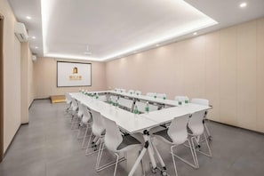 A conference room with a long table, white chairs, and a projector screen.
