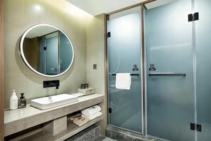 Une salle de bain moderne avec un grand miroir rond, un lavabo, une douche en verre et un porte-serviettes.