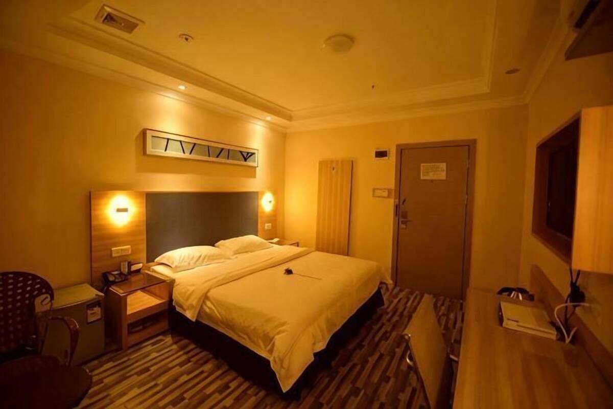 A hotel room with a double bed, bedside tables, a desk, a chair, a TV, and a door.