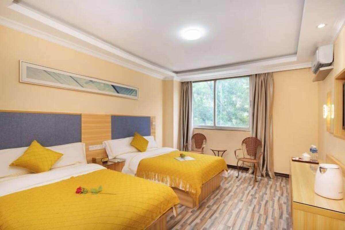 A hotel room with two beds, a desk, a chair, a window with curtains, and a painting on the wall.