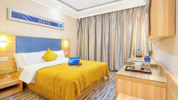Habitación de hotel con cama, mesitas de noche, escritorio con silla, ventana con cortinas y televisor montado en la pared.