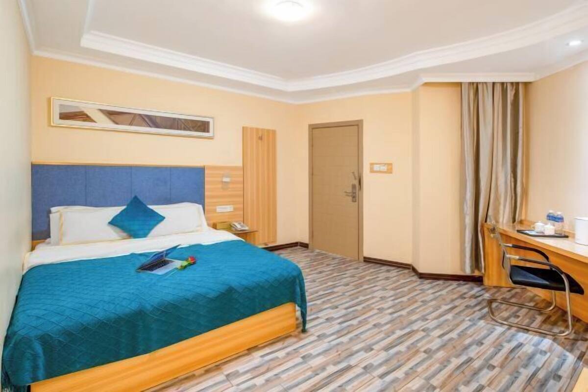 A hotel room with a bed, a desk, a chair, a door, and a window.