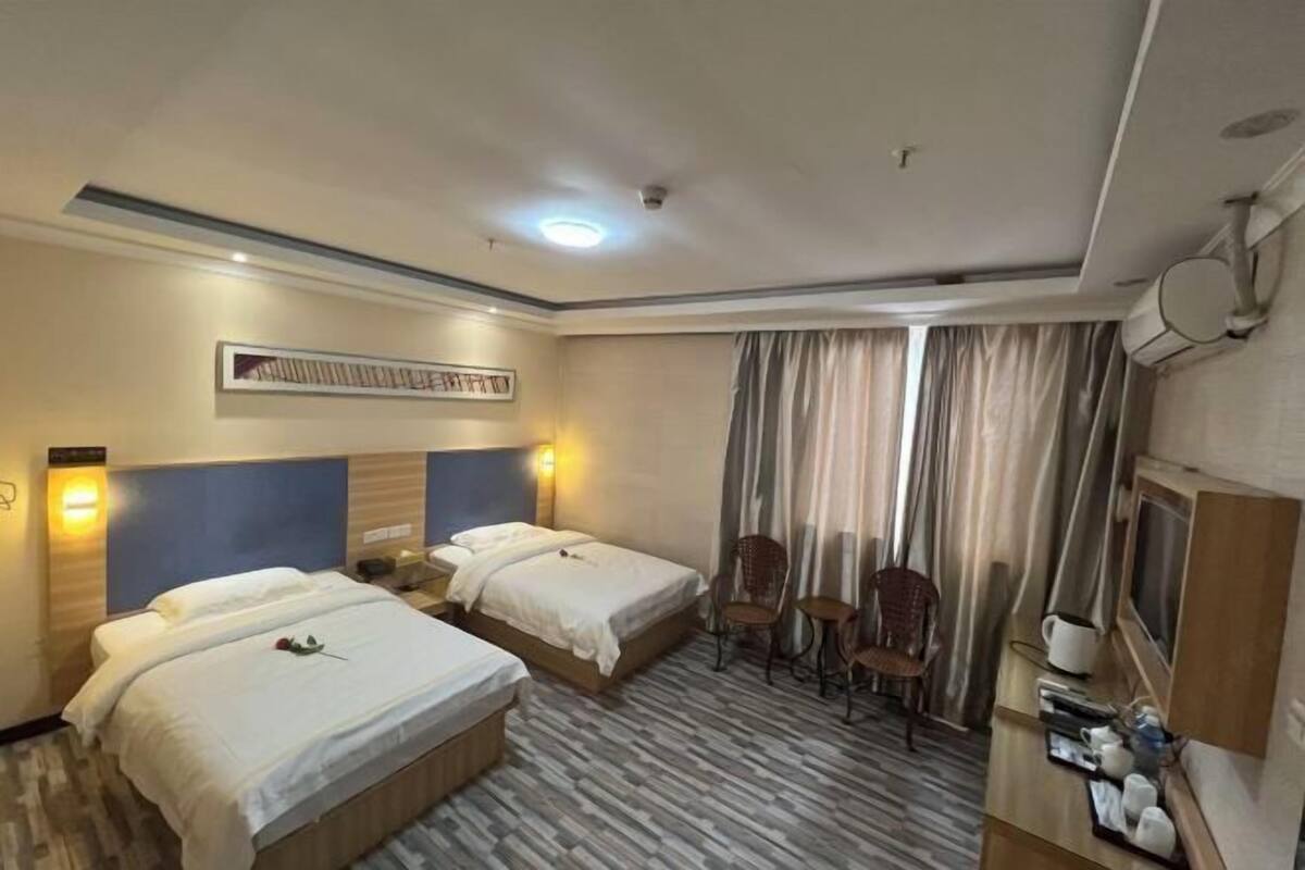 A hotel room with two beds, a desk with a chair, a television, and a window with curtains.