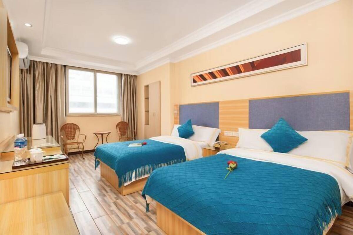 A hotel room with two beds, a desk, a chair, a window, and a mirror.