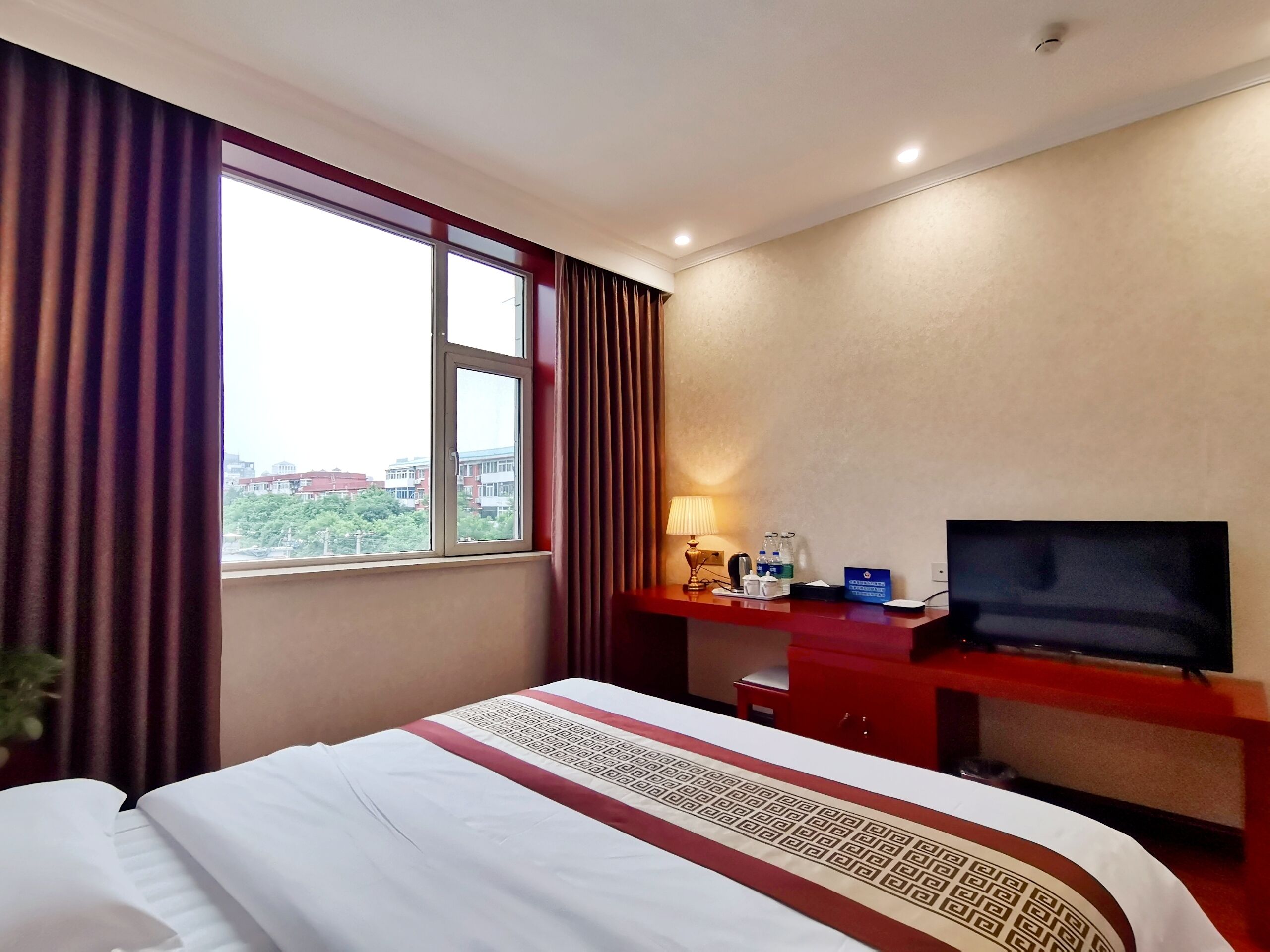Een hotelkamer met een bed, een bureau met een televisie, een lamp en een raam met gordijnen.