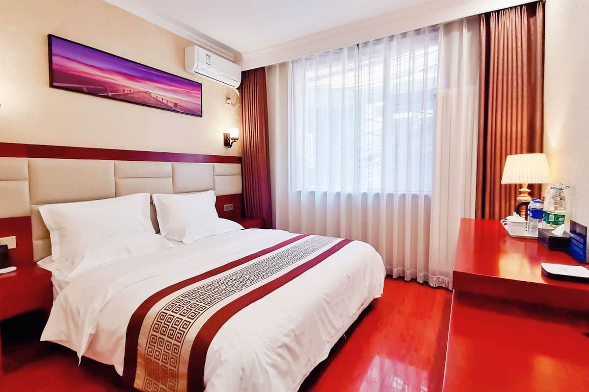 Une chambre d’hôtel avec un grand lit, une table de chevet, une lampe et une fenêtre avec des rideaux.
