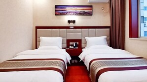 Hotellihuone, jossa on kaksi sänkyä, seinällä taulu, ilmastointilaite ja ikkuna, jossa on verhot.