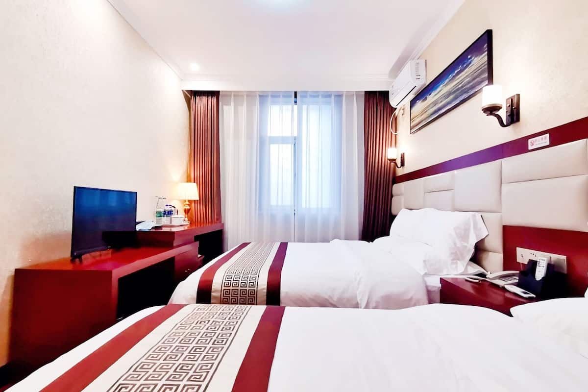 Une chambre d’hôtel avec deux lits, un bureau, une télévision et une fenêtre avec des rideaux.