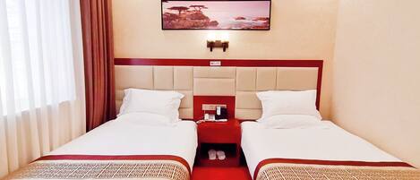 Habitación de hotel con dos camas, una alfombra roja, un cuadro en la pared y una mesita de noche con teléfono y cargador.
