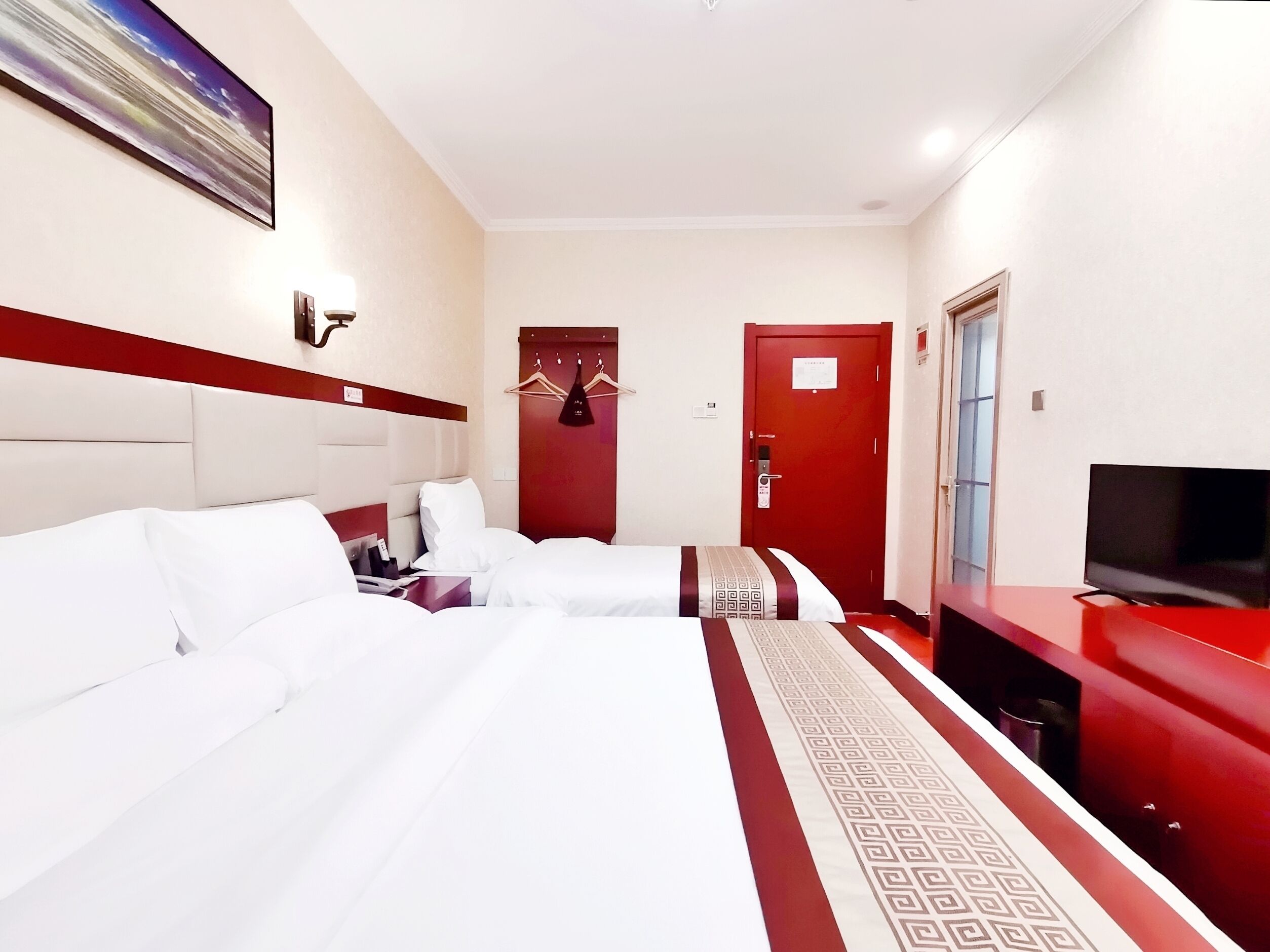 A hotel room with a large bed, a TV, a red door, and a painting on the wall.
