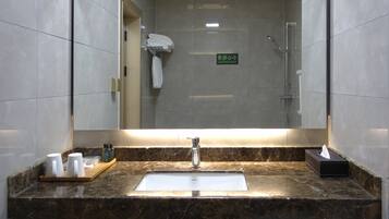 Un baño con un espejo grande, un lavabo y una ducha. Hay toallas colgadas en un perchero y un cartel en el espejo.