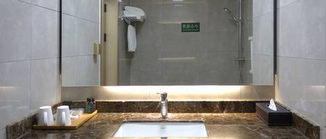 A bathroom with a large mirror, a sink, and a shower. There are towels hanging on a rack and a sign in the mirror.