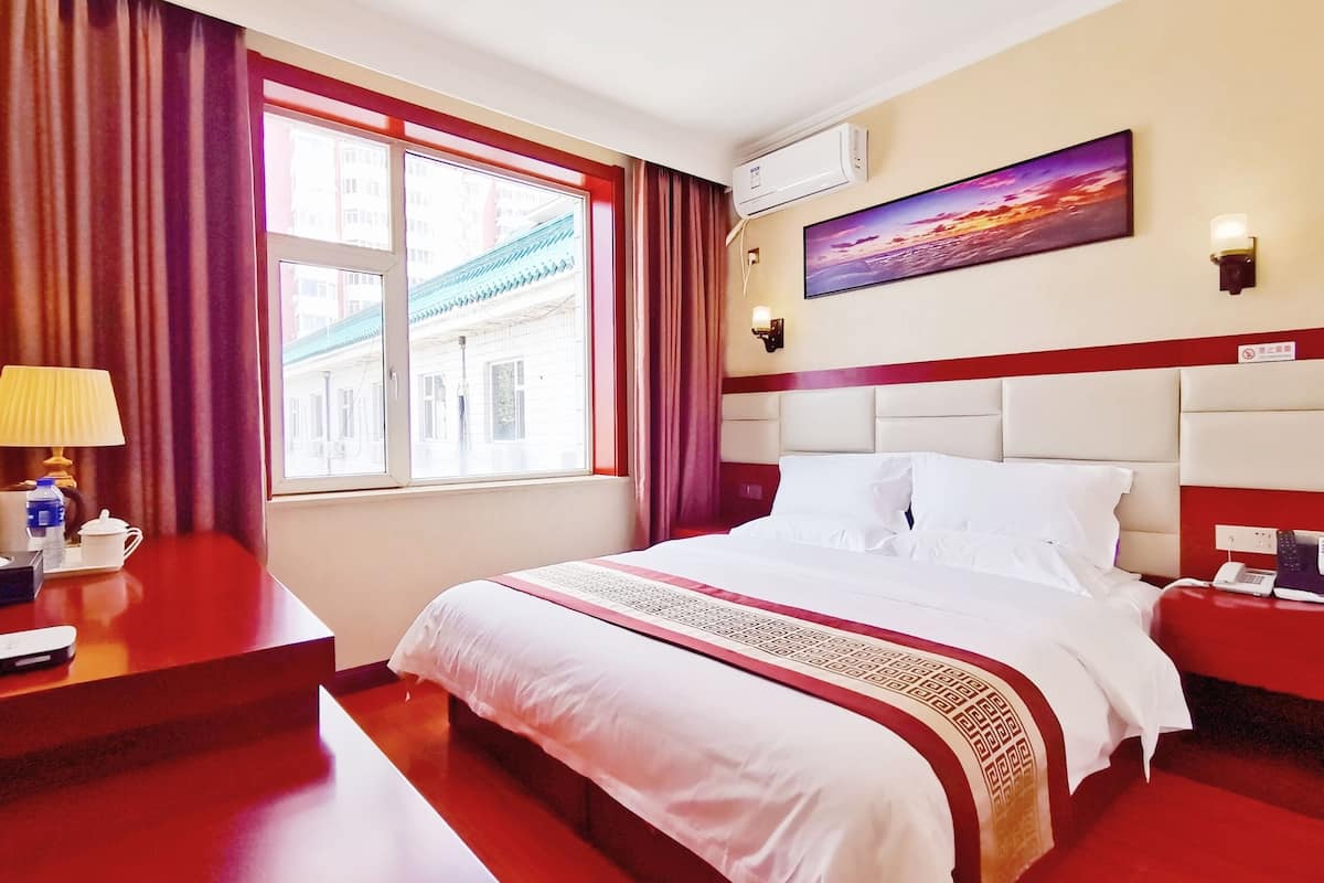 Une chambre d’hôtel avec un grand lit, un bureau avec une lampe, un tableau au mur et un appareil de climatisation.