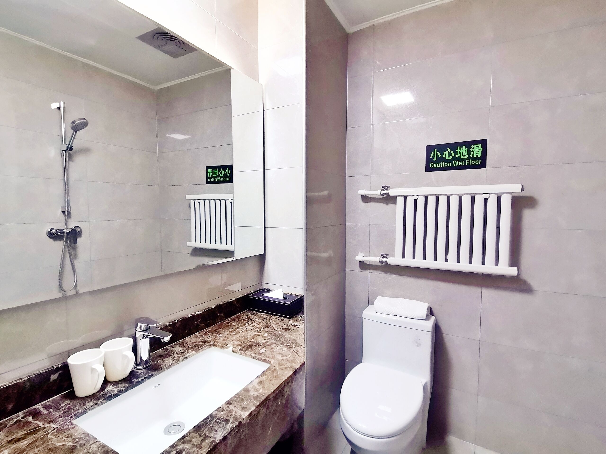 Un baño con lavamanos, dos tazas blancas, inodoro y ducha. Hay carteles en un idioma extranjero en las paredes.