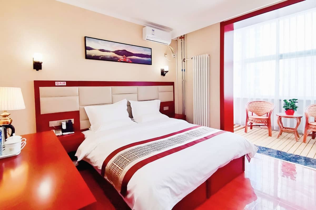 Une chambre d’hôtel comprenant un lit, un bureau, une chaise, une petite table avec une plante et un balcon avec des chaises.