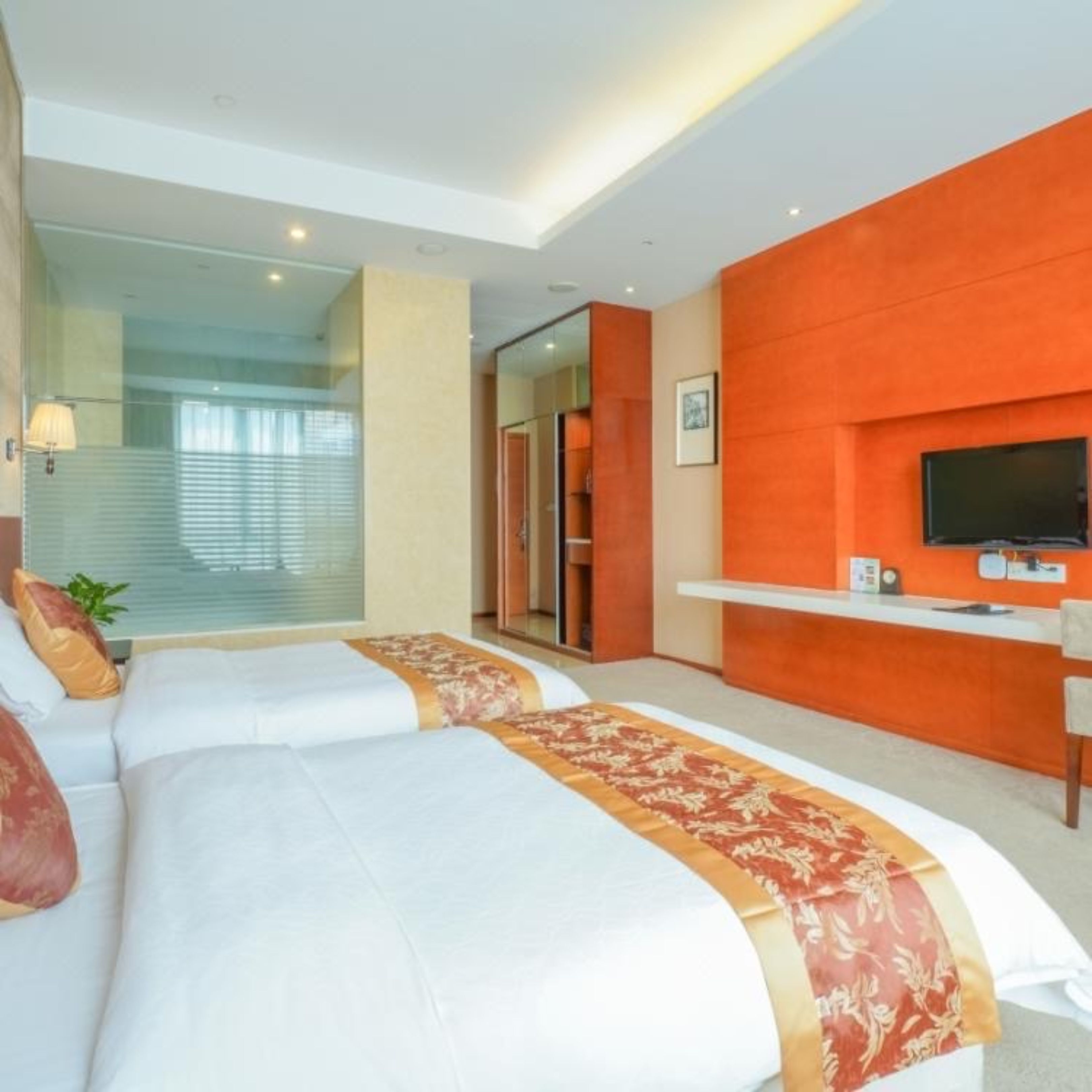 A hotel room with two beds, a TV on the wall, and a glass door leading to a balcony.