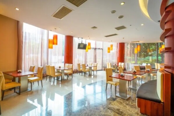 A hotel dining area with tables and chairs, large windows, and modern pendant lighting.