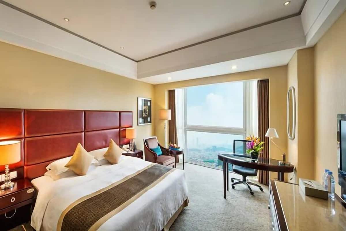 Ein Hotelzimmer mit einem großen Bett, einem Schreibtisch mit Fernseher und Blick auf die Stadt.