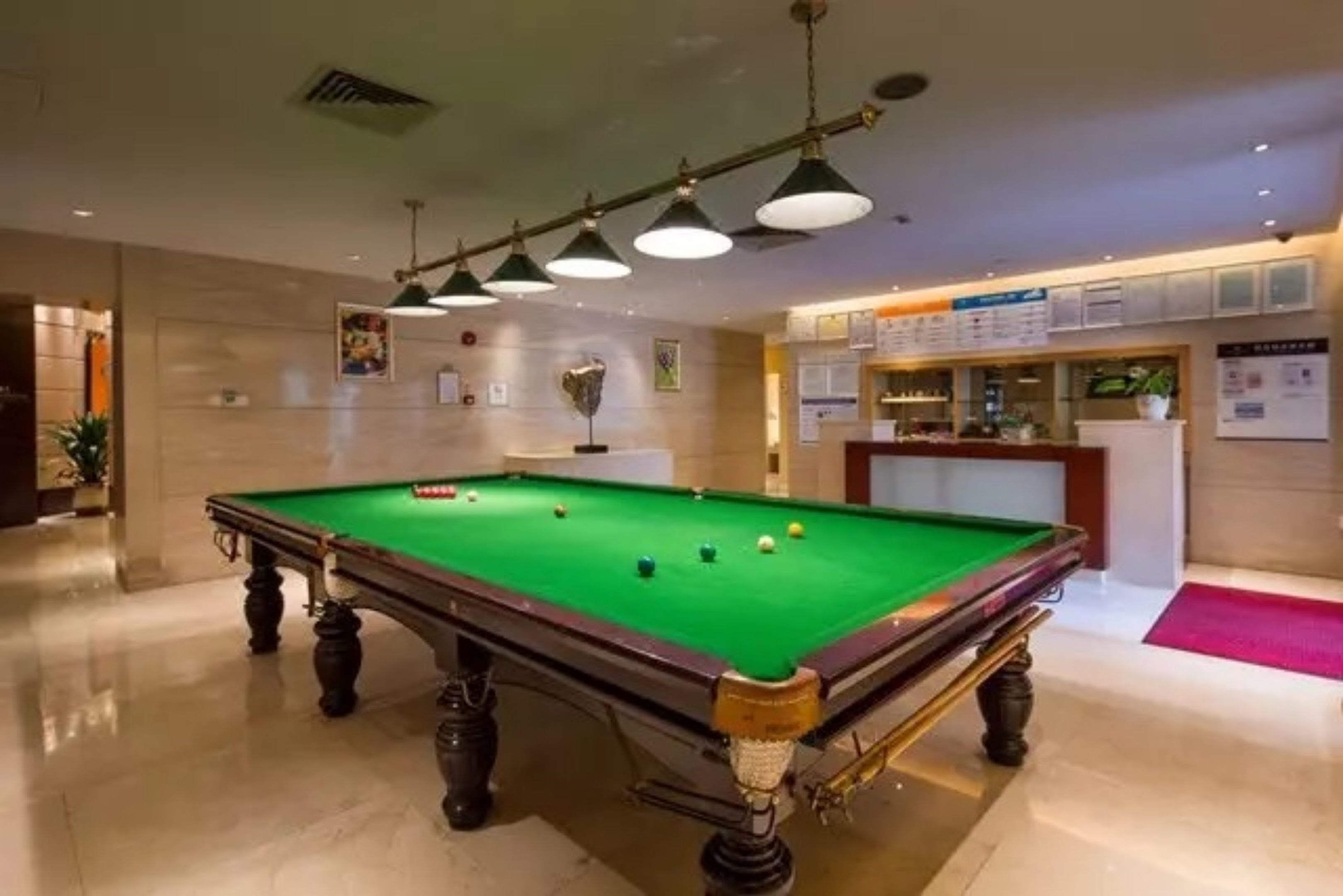 A pool table in a well-lit room with a marble floor, a reception desk, and a menu board.
