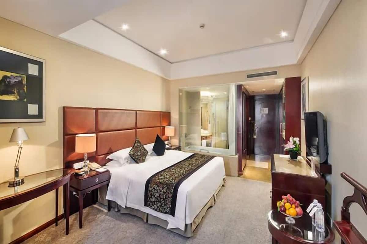 Ein Hotelzimmer mit einem großen Bett, Nachttischen, einem Schreibtisch, einem Spiegel und einem Fernseher.