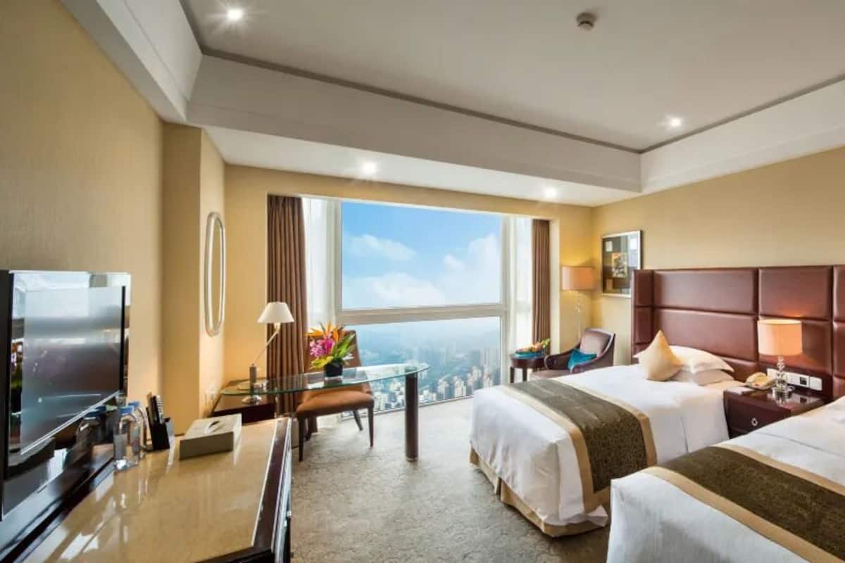 Ein Hotelzimmer mit zwei Betten, einem Schreibtisch mit Fernseher und Blick auf die Stadt.