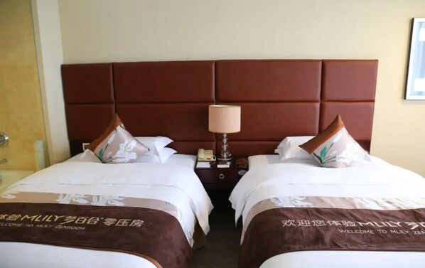 Habitación de hotel con dos camas, cada una con cabecero marrón y almohada a juego. Entre las camas, una mesita de noche con lámpara y teléfono.