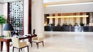 Um saguão de hotel com balcão de recepção, uma parede com taças de vinho e uma área de refeições com mesa e cadeiras.