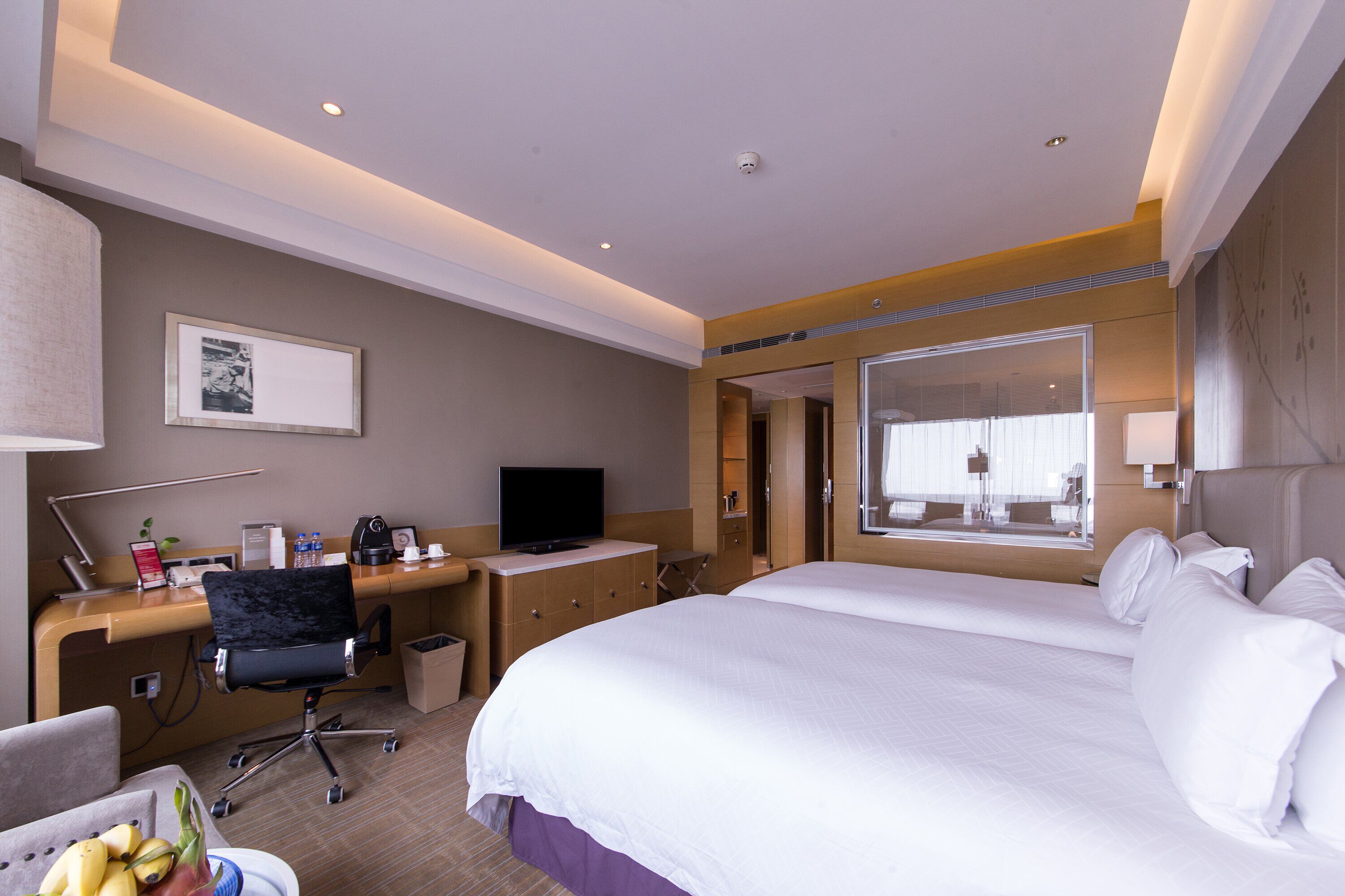 Habitación de hotel con una cama grande, un escritorio con computadora, una silla, un televisor y una ventana con persianas.