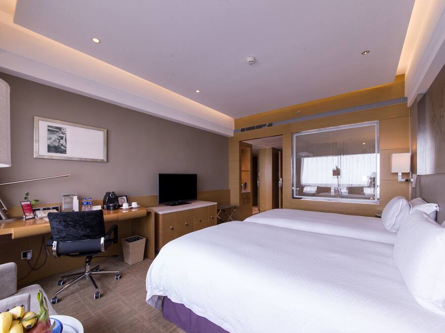 Habitación de hotel con una cama grande, un escritorio con computadora, una silla, un televisor y una ventana con persianas.
