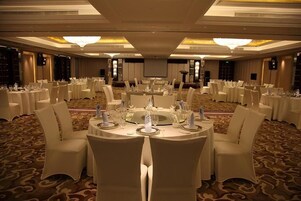 A banquet hall with round tables set for dining, white chairs, and a carpeted floor.