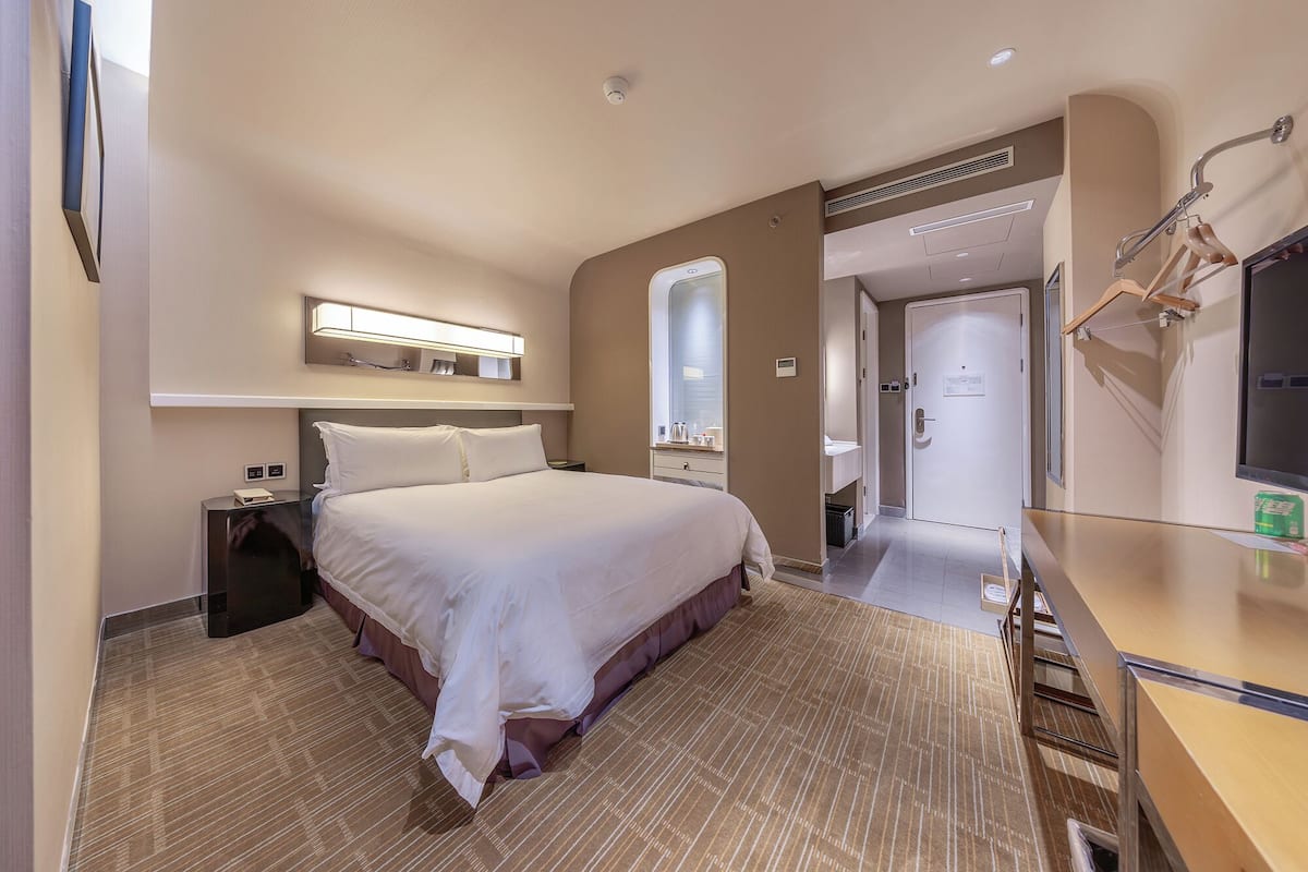 Ein Hotelzimmer mit einem großen Bett, Nachttischen, einem Spiegel, einem Schreibtisch und einem Kleiderschrank.