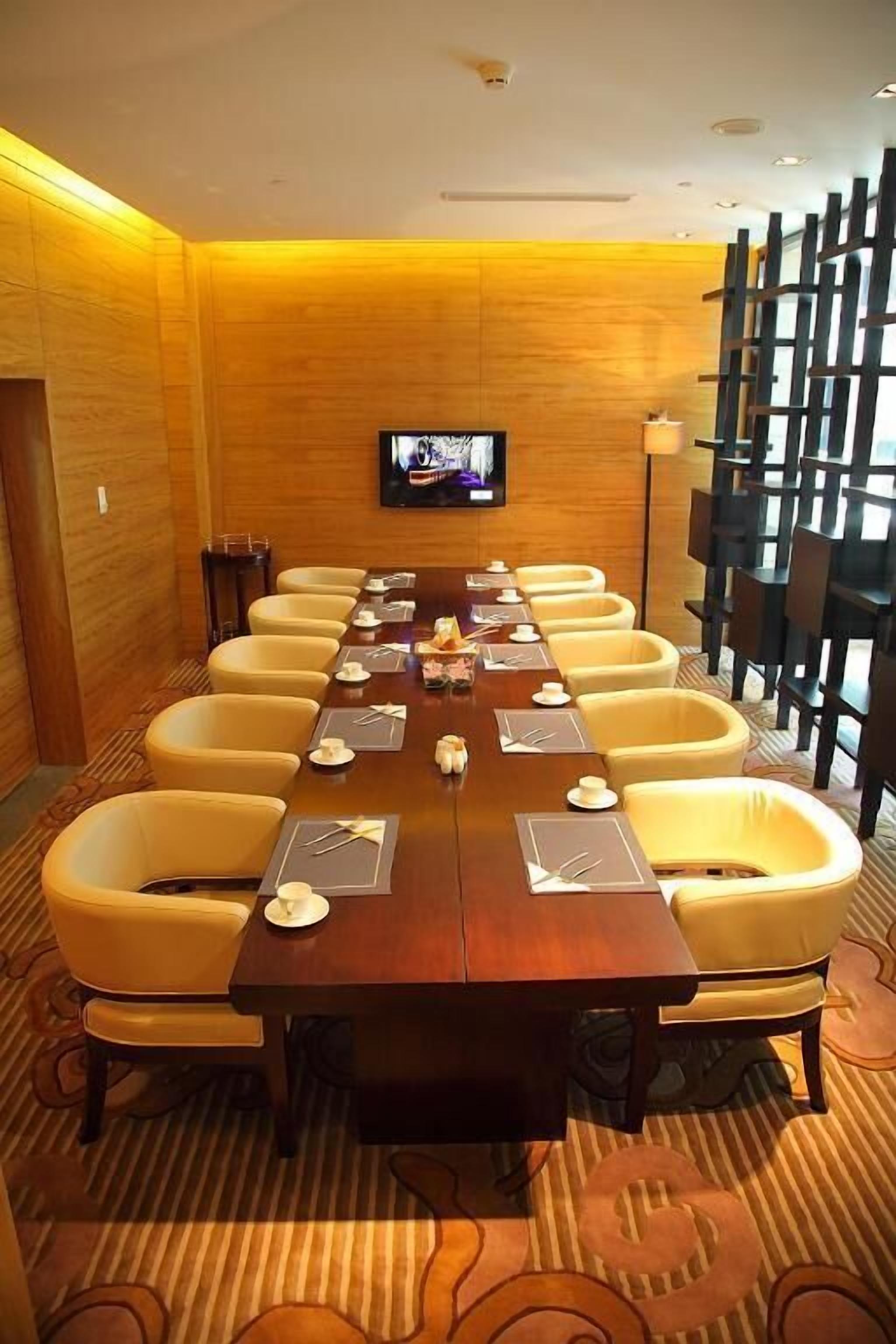 Une salle de conférence avec une longue table, des chaises jaunes et un téléviseur fixé au mur.