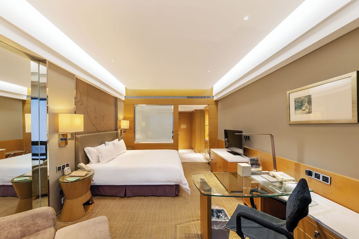 Ein Hotelzimmer mit zwei Betten, einem Schreibtisch, einem Sessel, einem Fernseher und einem großen Fenster.