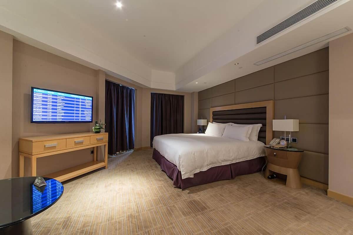 Ein Hotelzimmer mit Bett, Nachttisch, Lampe, Fernseher und Schreibtisch mit Stuhl.