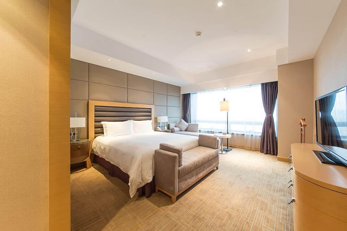 Ein modernes Hotelzimmer mit einem großen Bett, einer Couch, einem Fernseher und einem Schreibtisch.