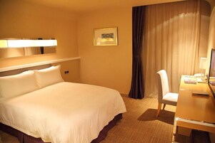 A hotel room with a large bed, a desk with a chair, a lamp, and a framed picture on the wall.