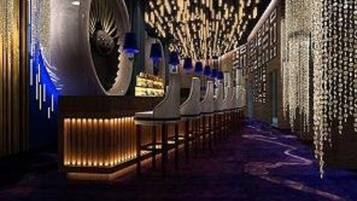 A corridor with a series of uniformly lit columns, a large cylindrical structure on the left, and a patterned ceiling.