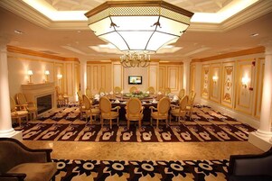 A formal meeting room with a large oval table, multiple chairs, a chandelier, and a television screen.