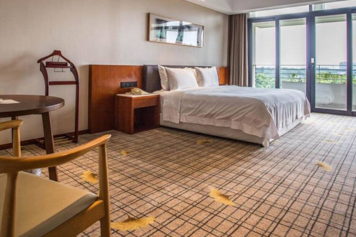A hotel room with a bed, a desk, a chair, a nightstand, and a large window with a view.