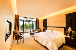 A hotel room with a large bed, a desk with a chair, a small table, and a window with curtains.