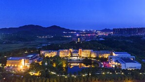 A hotel with multiple buildings, a large parking area, and a body of water in the foreground. - Preess Resort Hotel (Changsha)